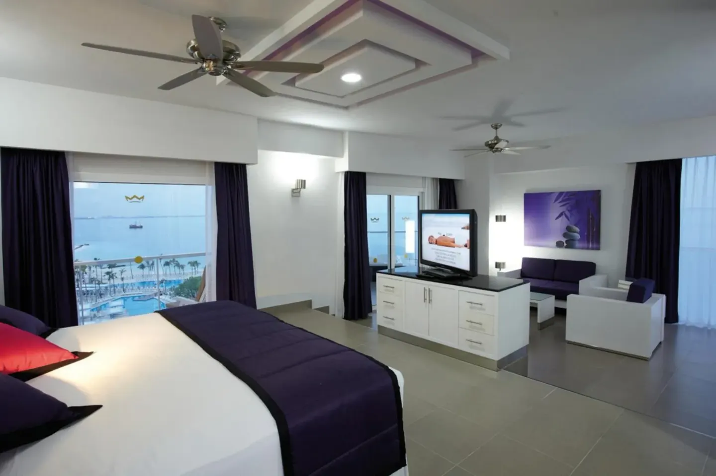 Guest room with a king bed, seating area, TV and water view at Hotel Riu Palace Peninsula.