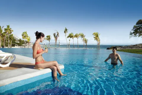 Guests relax by the oceanfront pool at Hotel Riu Palace Peninsula.