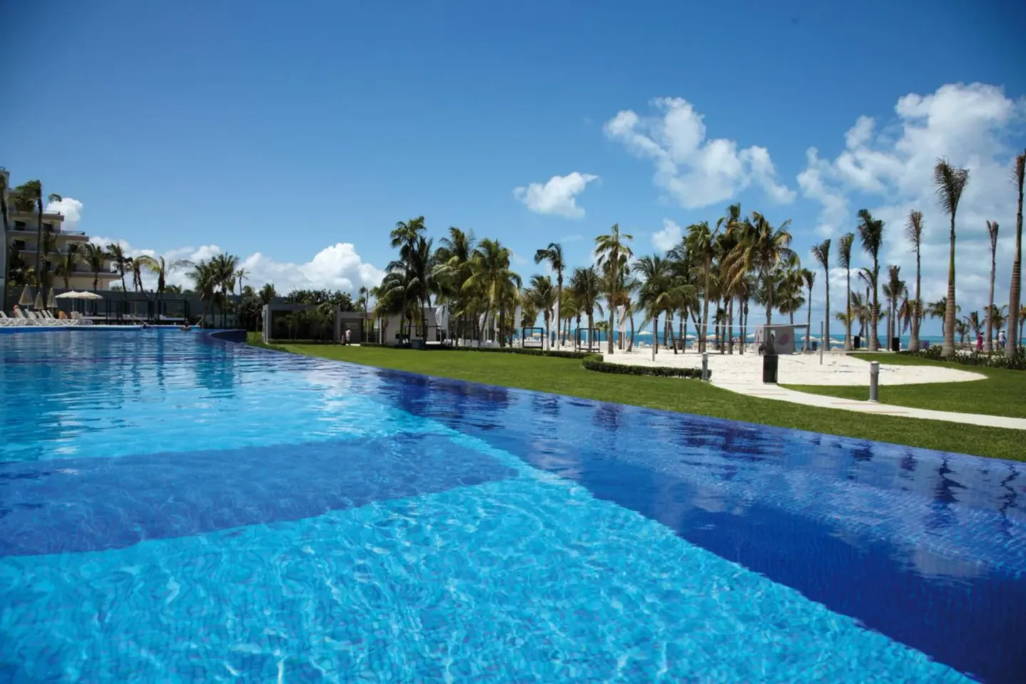 Large blue pool beside lawns, palms, and beach at Hotel Riu Palace Peninsula.