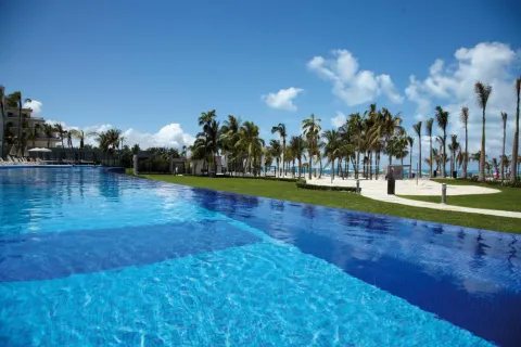 Large blue pool beside lawns, palms, and beach at Hotel Riu Palace Peninsula.