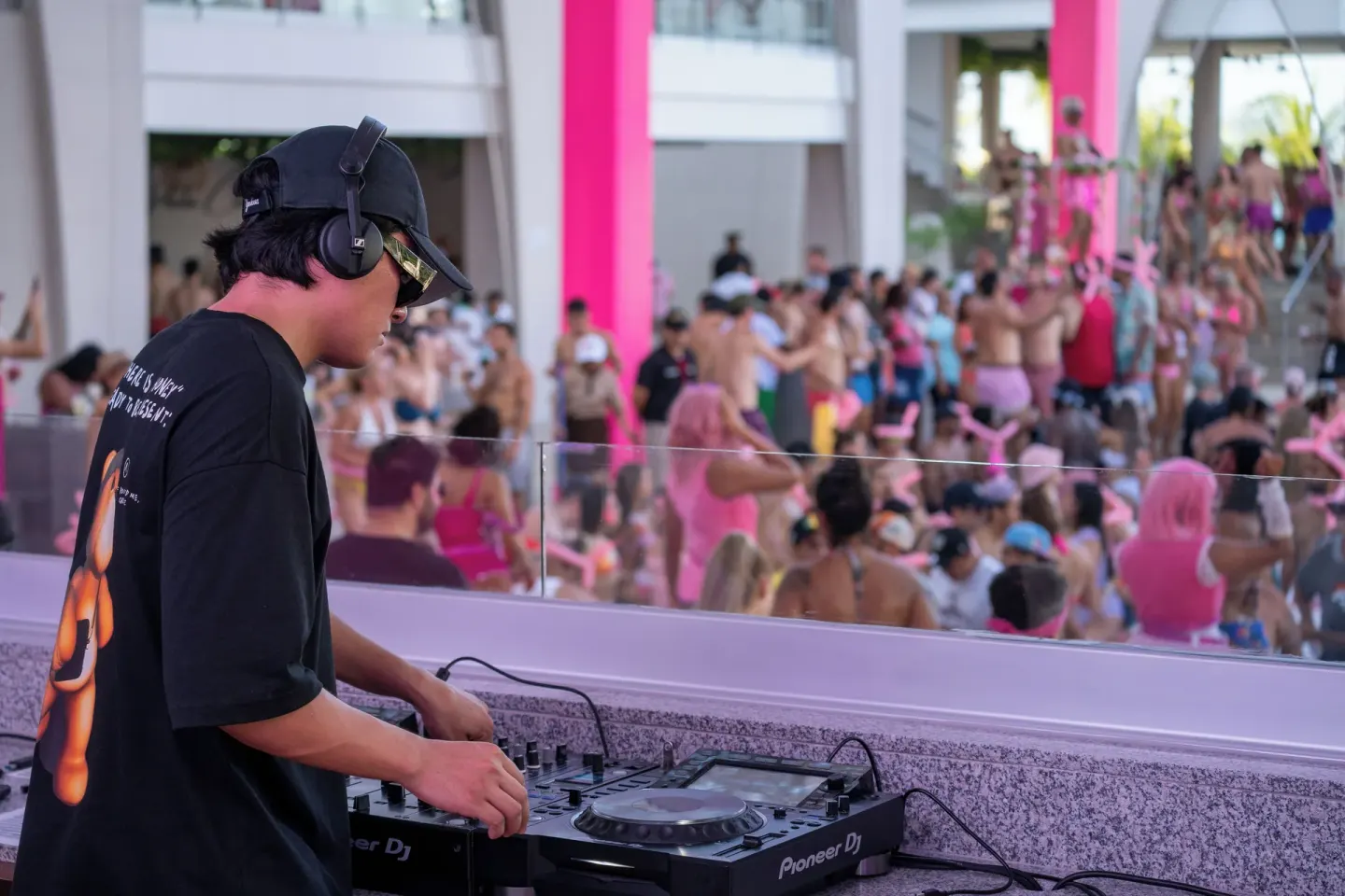 A DJ works at a console above a busy pool party at Hotel Riu Palace Peninsula.