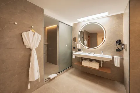 Elite Club Suite bathroom with double vanity, robe, and glass shower at Hotel Riu Palace Peninsula.