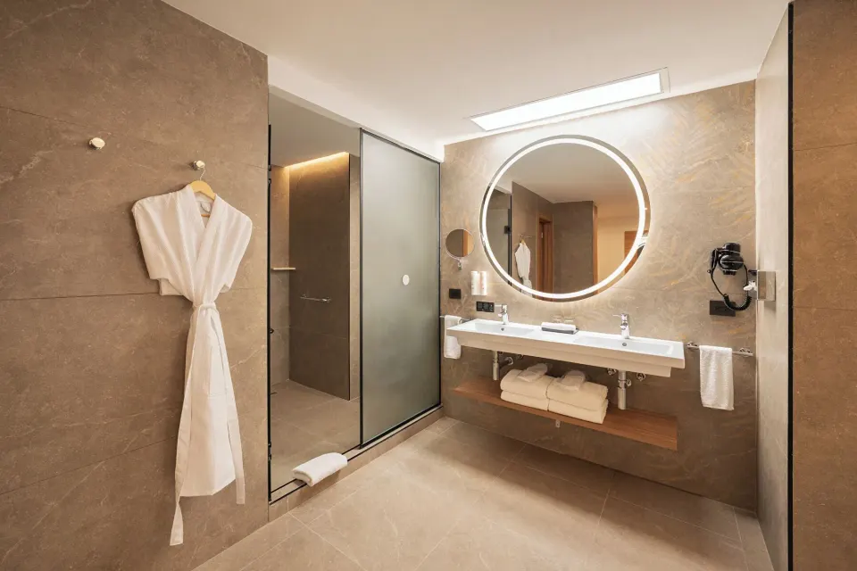 Elite Club Suite bathroom with double vanity, robe, and glass shower at Hotel Riu Palace Peninsula.