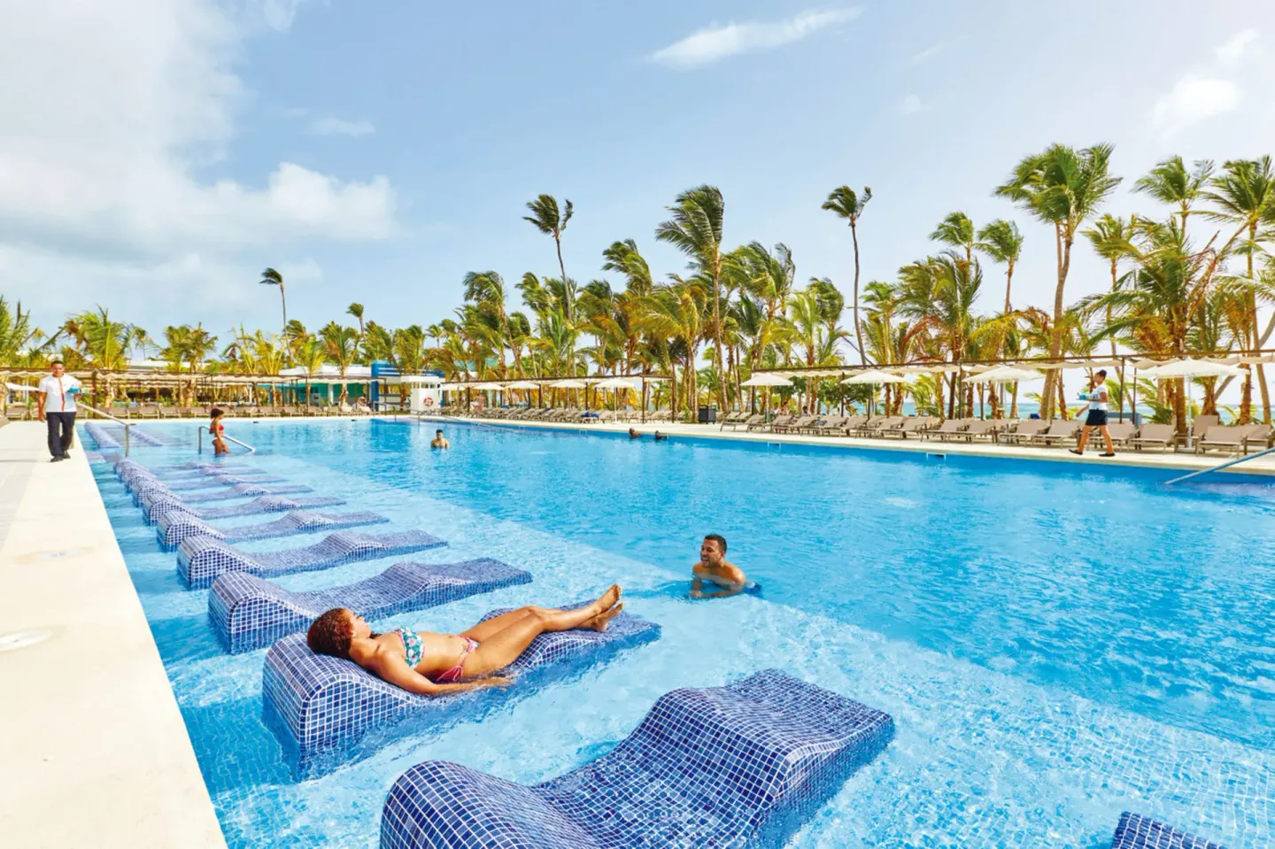 Large palm-lined pool with tiled water loungers at Hotel Riu Palace Punta Cana.