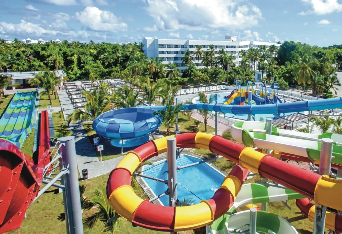Colorful water slides and pools beside a resort building at Hotel Riu Palace Punta Cana.