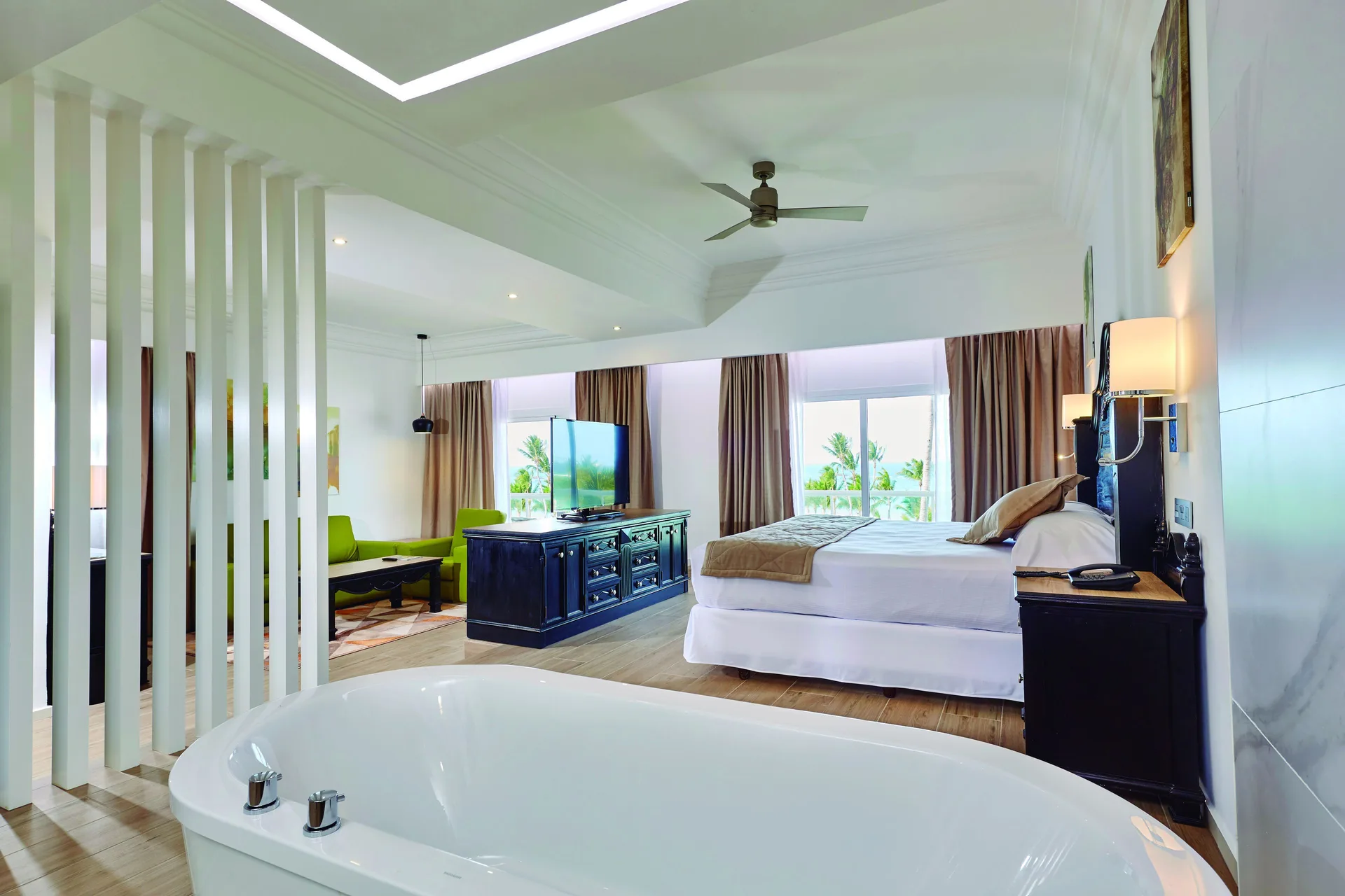Suite with king bed, freestanding tub, sitting area, and balcony light at Hotel Riu Palace Punta Cana.