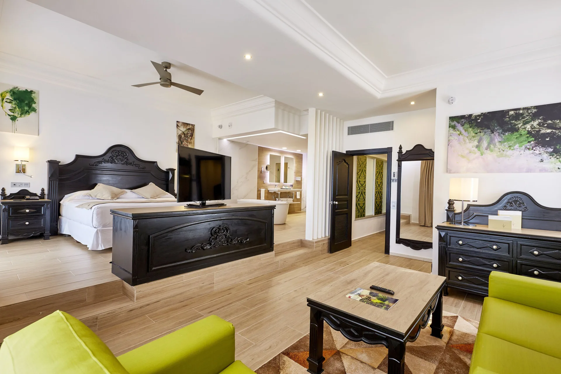 Suite with king bed, lounge area, TV, and open bathroom at Hotel Riu Palace Punta Cana.