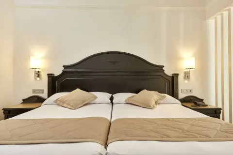 Suite bed at Hotel Riu Palace Punta Cana with dark headboard, bedside tables, wall lamps, and beige throws.