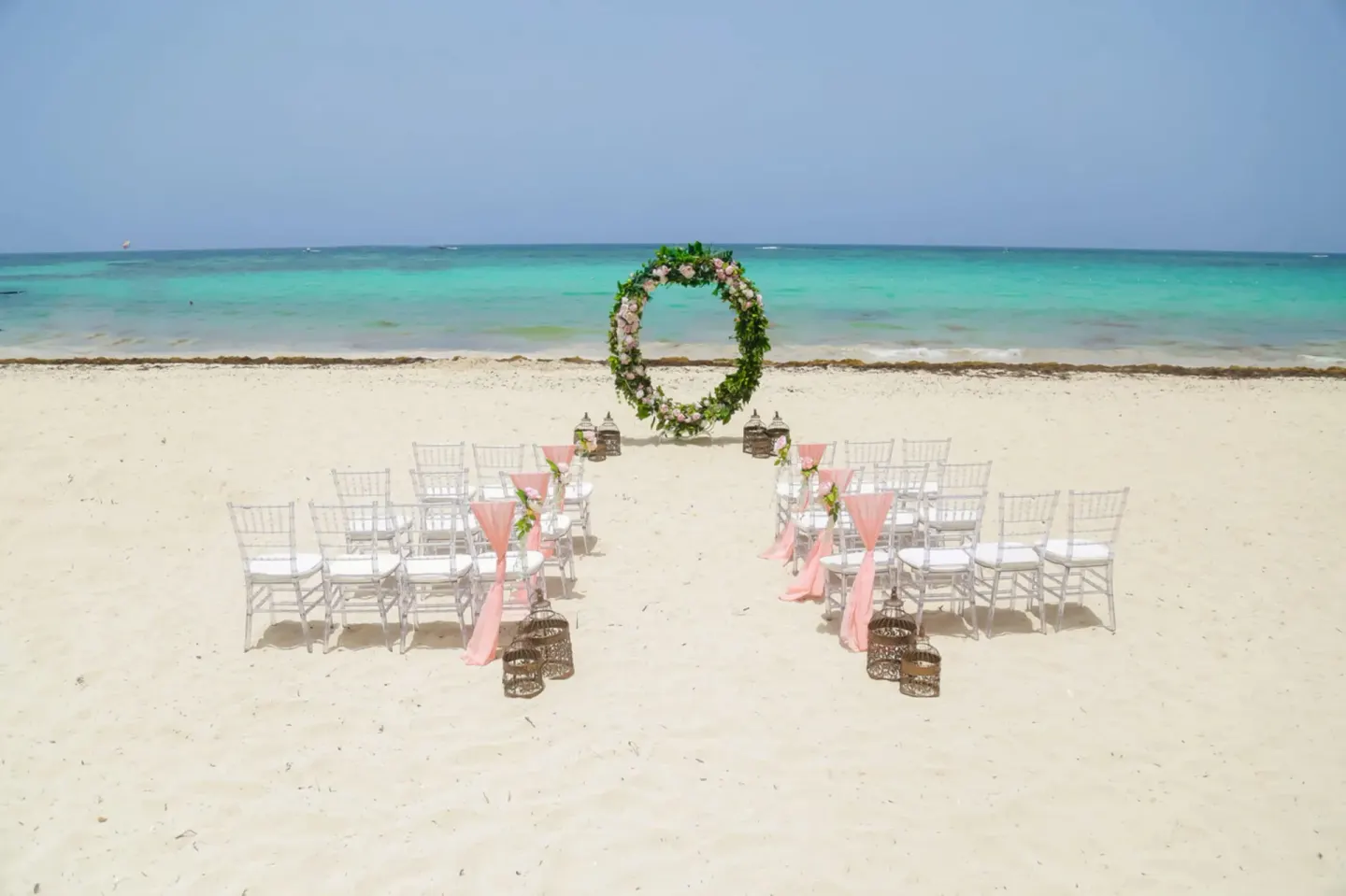 Beach wedding setup with white chairs and floral arch at Hotel Riu Palace Punta Cana.