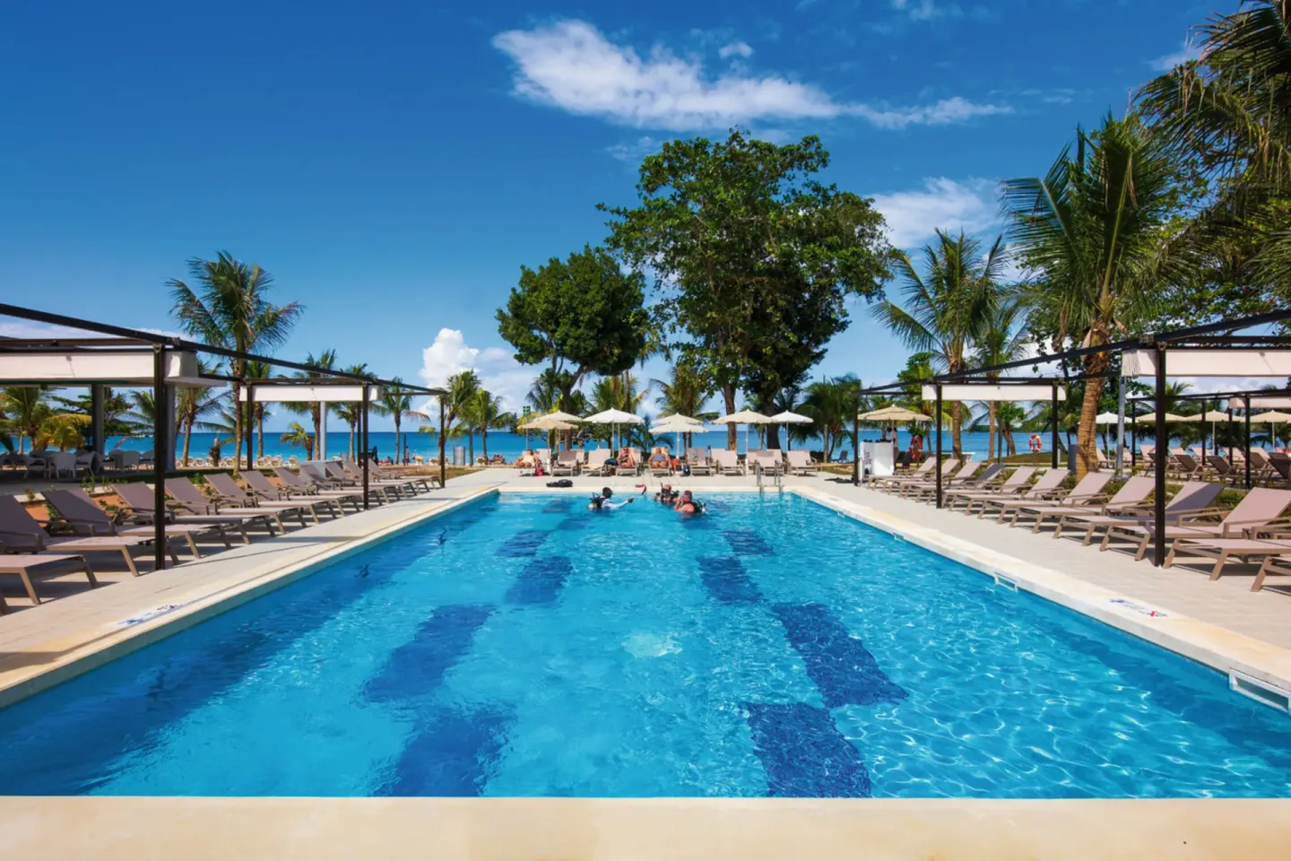 Beachfront pool with loungers and sea beyond at Hotel Riu Palace Tropical Bay.
