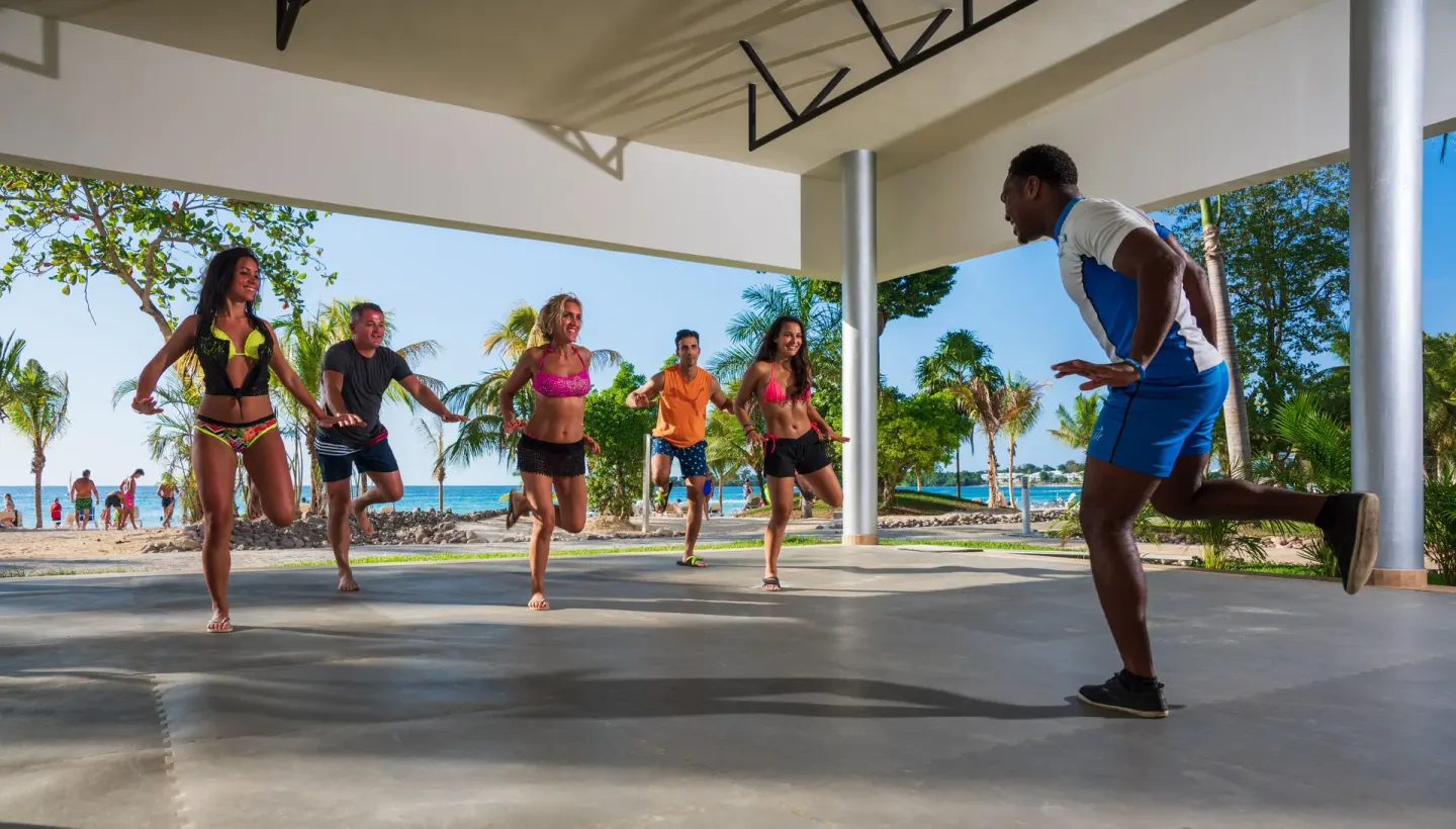 Group fitness class in an open pavilion by the beach at Hotel Riu Palace Tropical Bay.