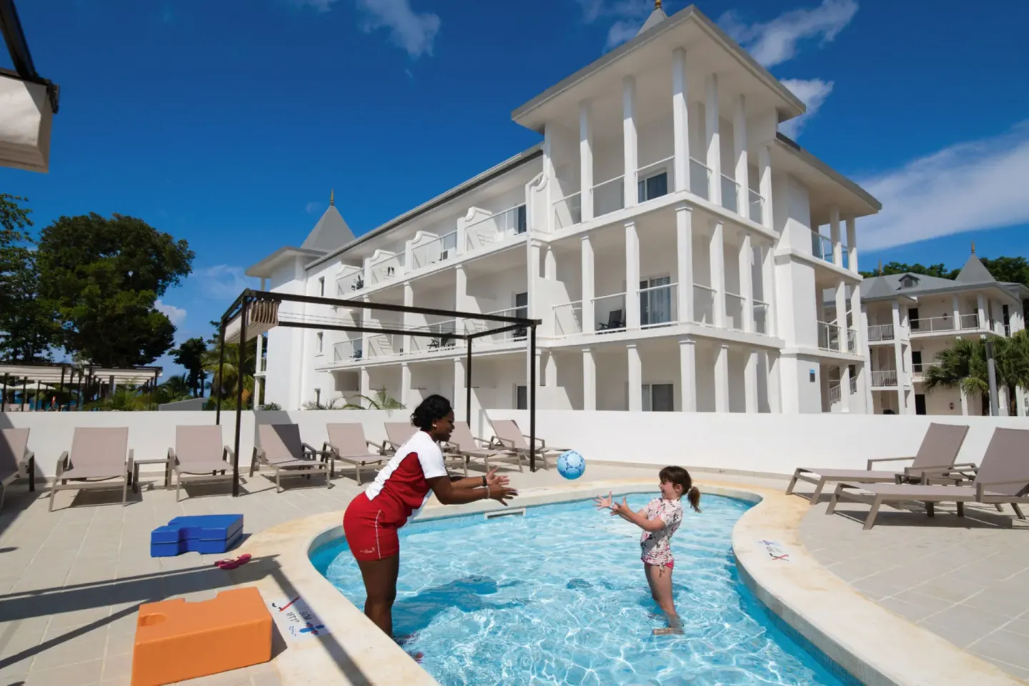 Children's pool activity beside white resort buildings at Hotel Riu Palace Tropical Bay.