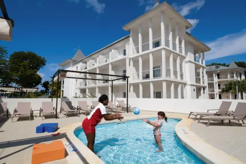 Children's pool activity beside white resort buildings at Hotel Riu Palace Tropical Bay.