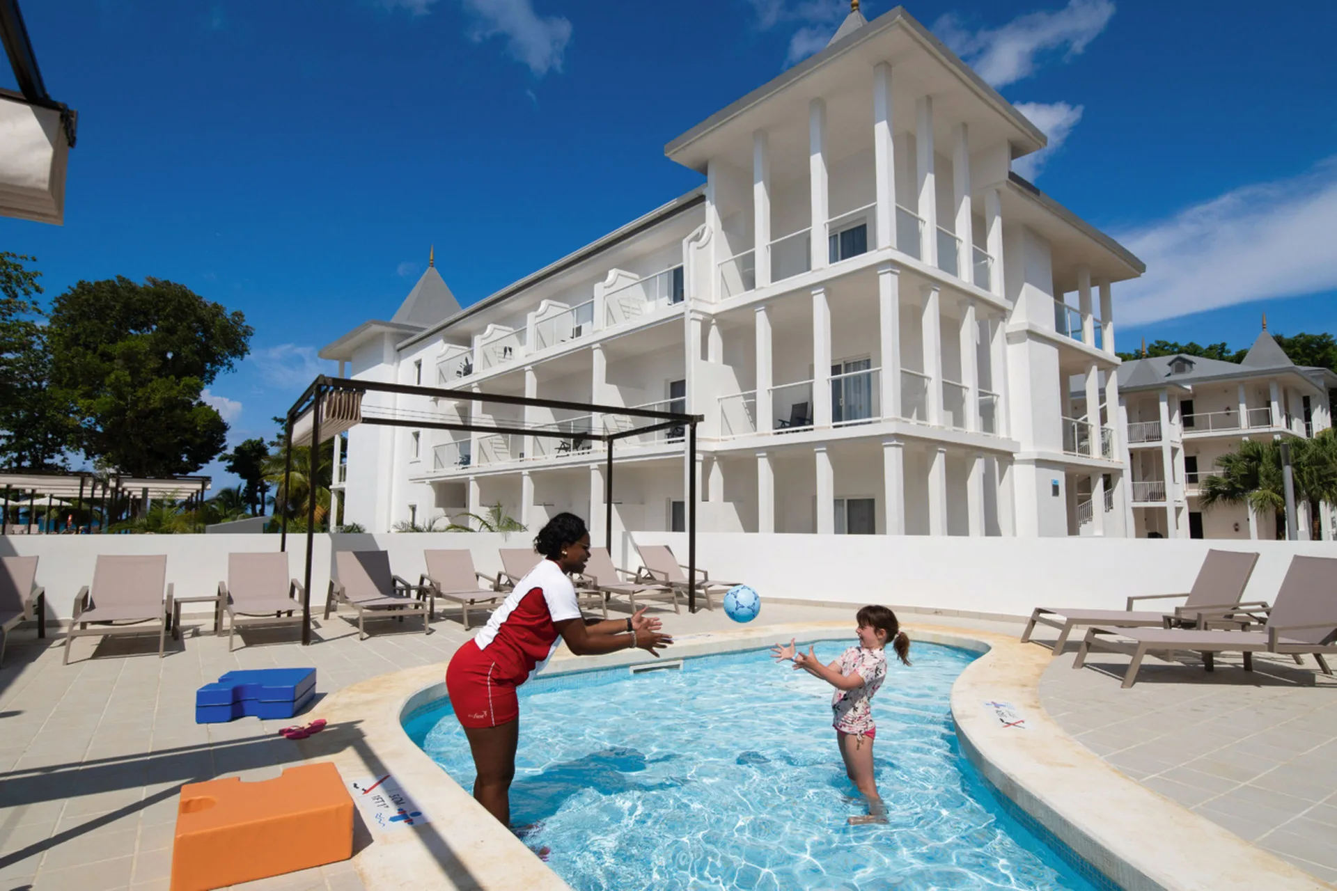 Children's pool activity beside white resort buildings at Hotel Riu Palace Tropical Bay.