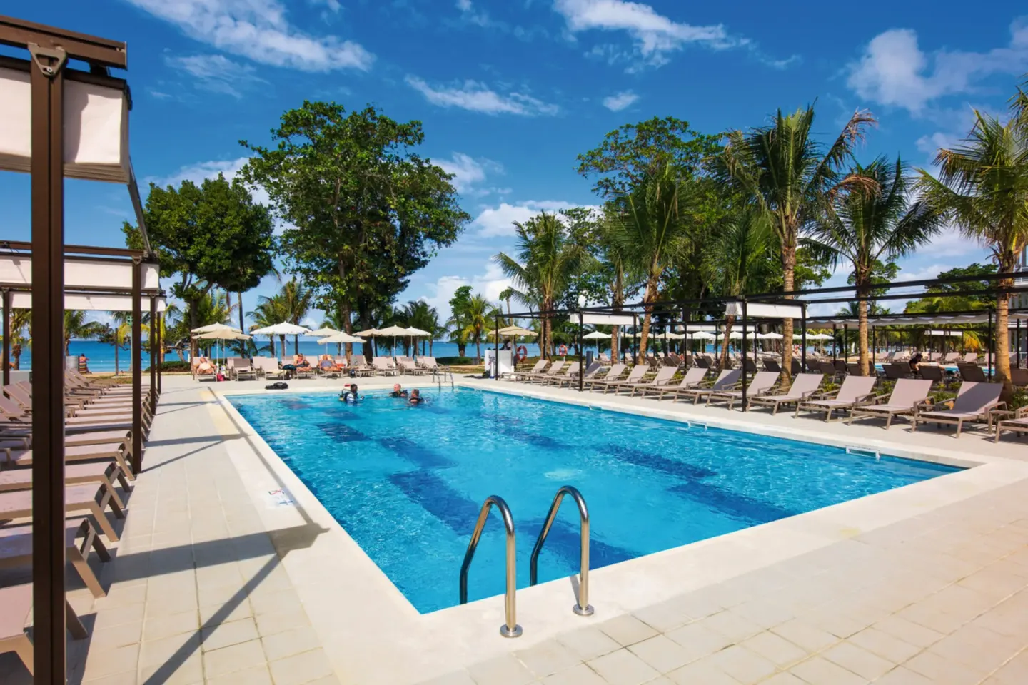 Long pool with pergola shade and ocean beyond at Hotel Riu Palace Tropical Bay.