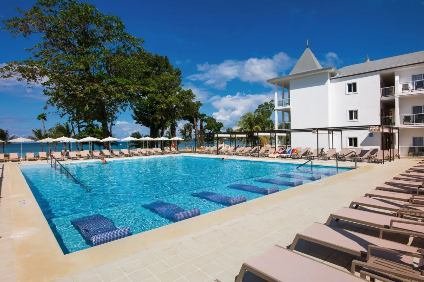 Pool beside white guestroom building at Hotel Riu Palace Tropical Bay.