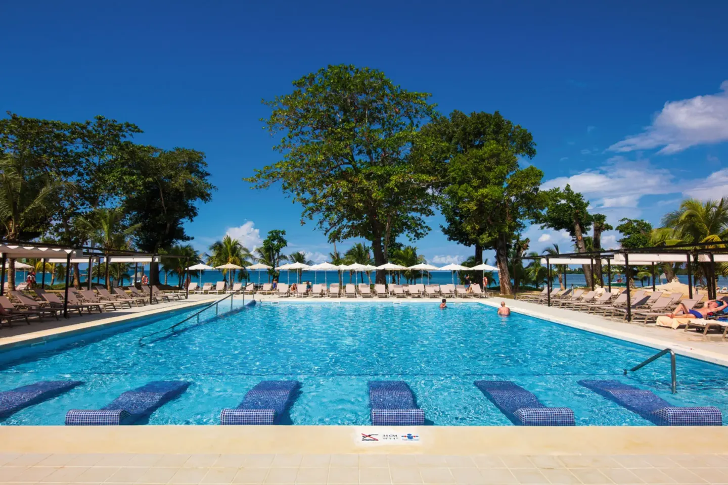 Wide pool view with in-water loungers and ocean backdrop at Hotel Riu Palace Tropical Bay.