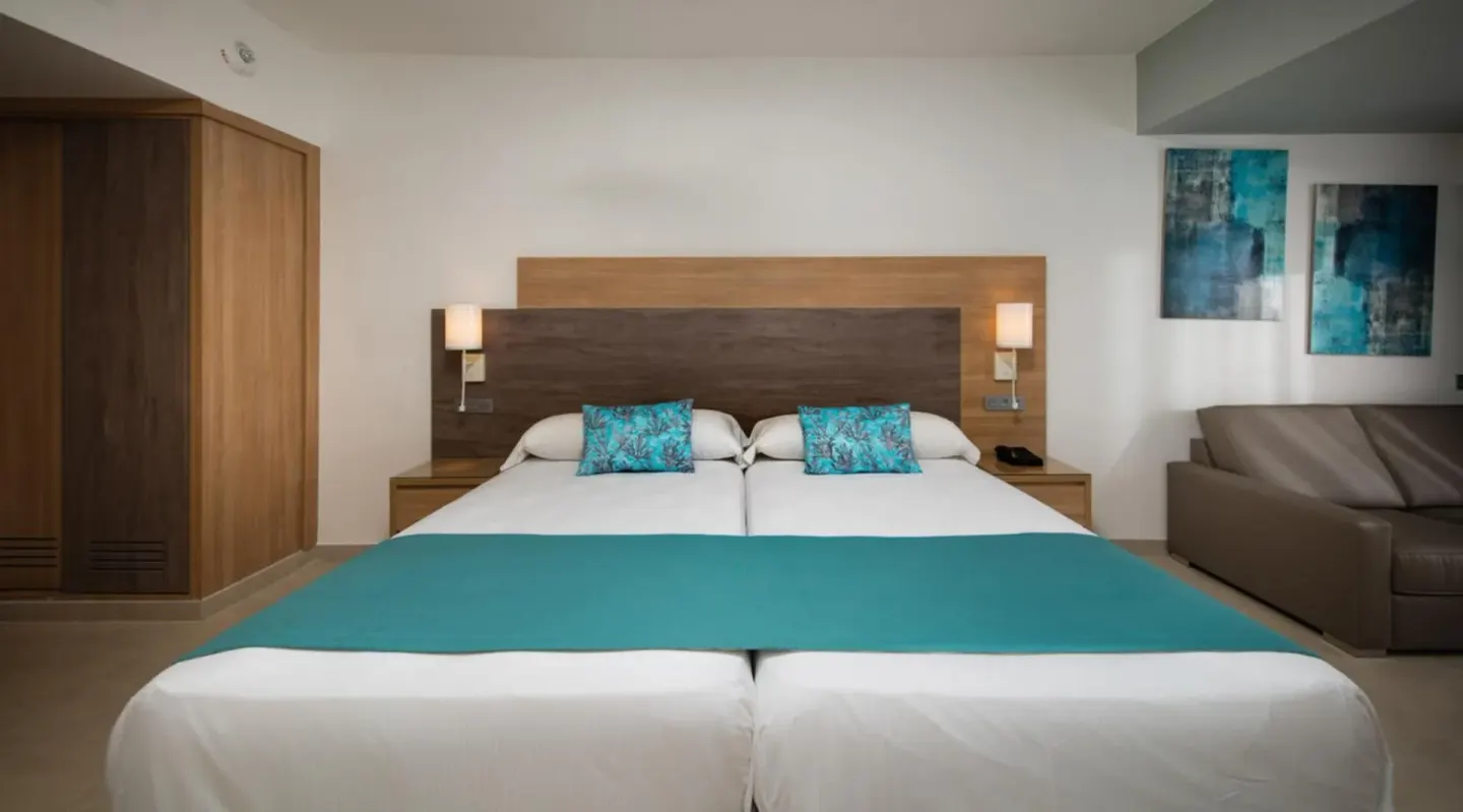 Junior Suite Garden View bed with sofa and wardrobe at Hotel Riu Palace Tropical Bay.