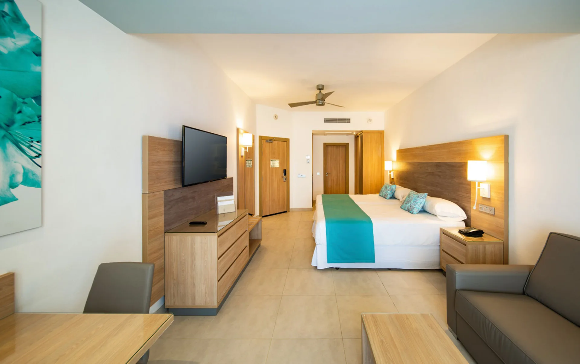 Junior Suite Garden View room with bed, sofa, TV, and wood furniture at Hotel Riu Palace Tropical Bay.