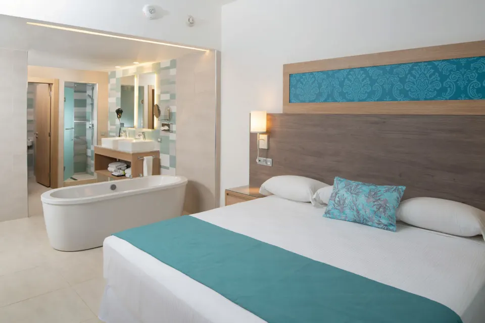 Ocean View suite king bed beside an open bath area at Hotel Riu Palace Tropical Bay.