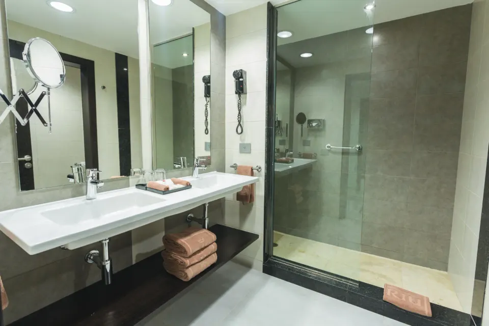 Bathroom with double sink, large mirror and glass-enclosed shower at Hotel Riu Playacar