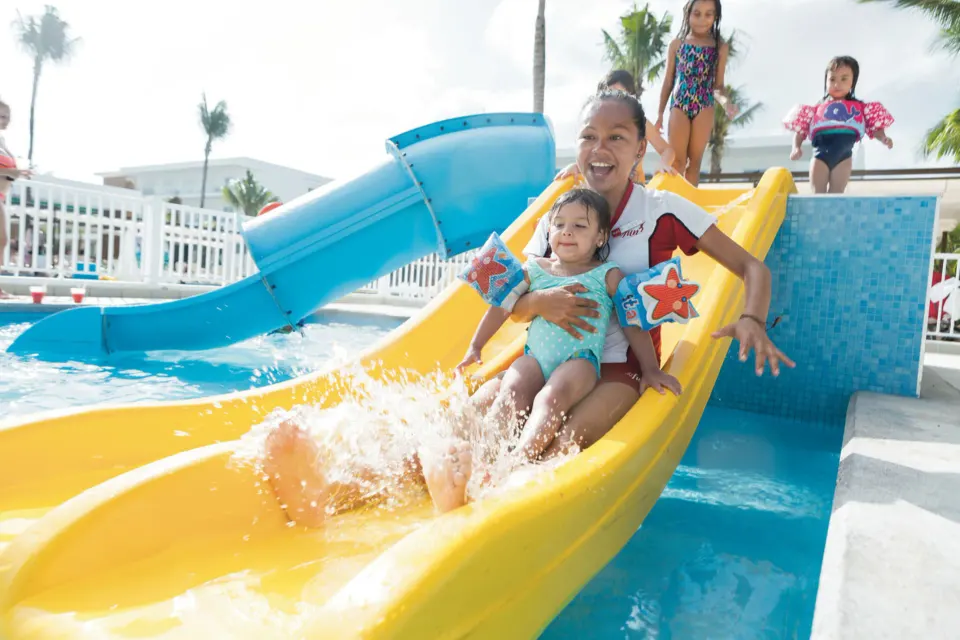 Family sliding down a yellow water slide into a pool at Hotel Riu Playacar