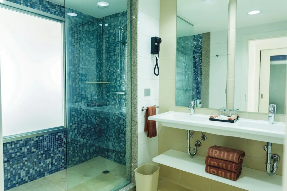Glass shower with blue mosaic tile next to a sink in a guest room at Hotel Riu Playacar