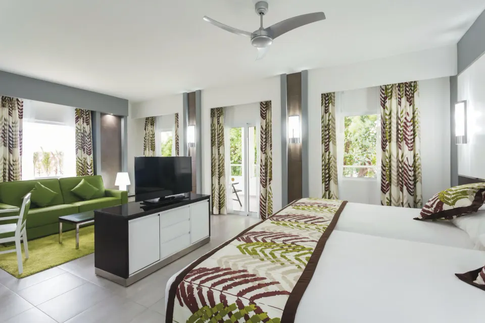 Spacious suite with king bed, seating area and TV at Hotel Riu Playacar.