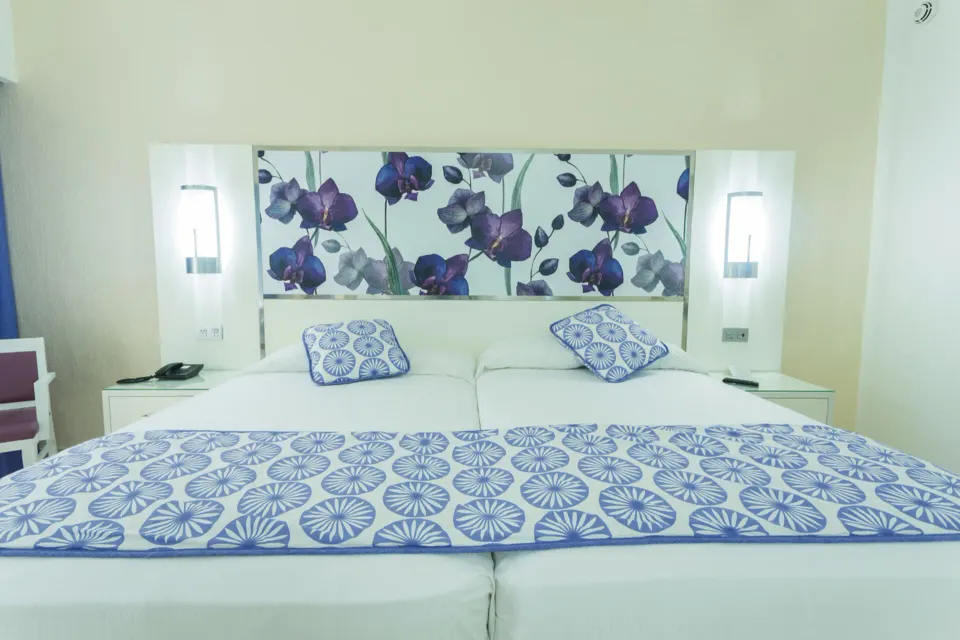 Close-up of king bed with floral headboard and patterned runner in a room at Hotel Riu Playacar