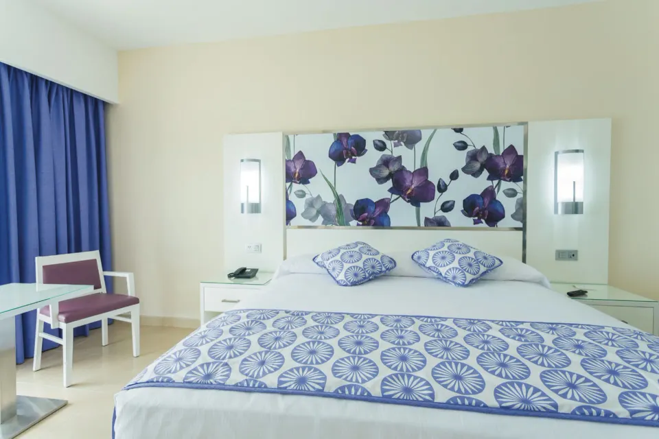 Front view of king bed with purple curtains and seating area in a room at Hotel Riu Playacar