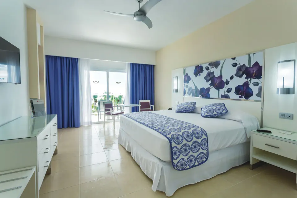 Spacious guest room with king bed, balcony doors and tiled floor at Hotel Riu Playacar