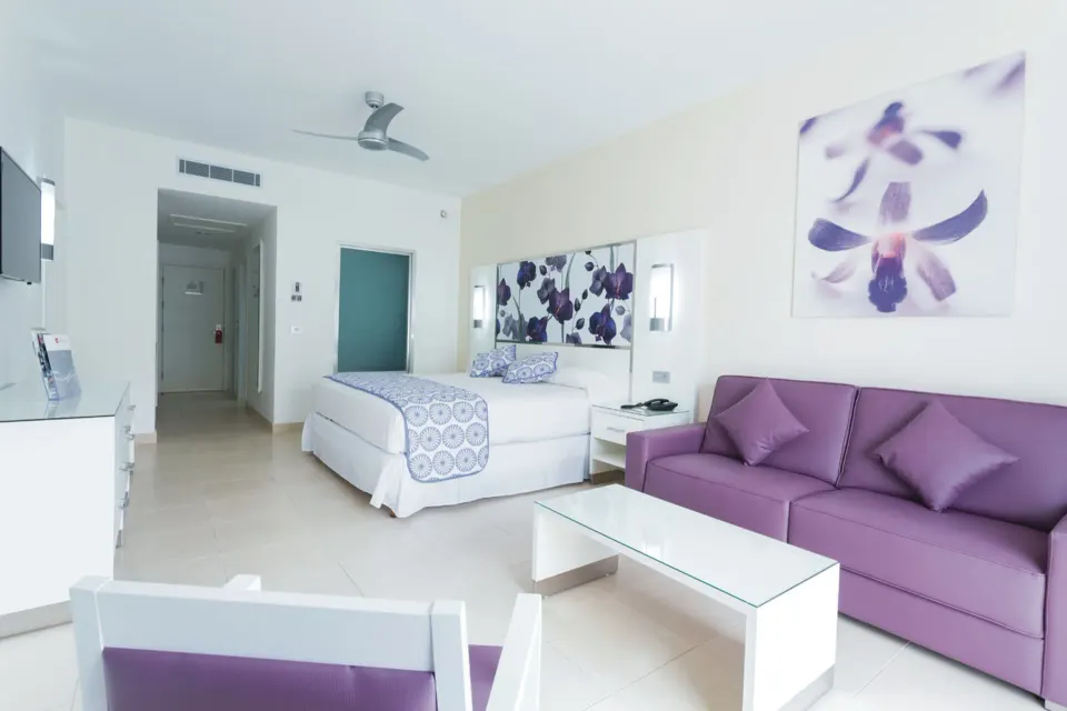 Bright suite with king bed, purple sofa and seating area at Hotel Riu Playacar