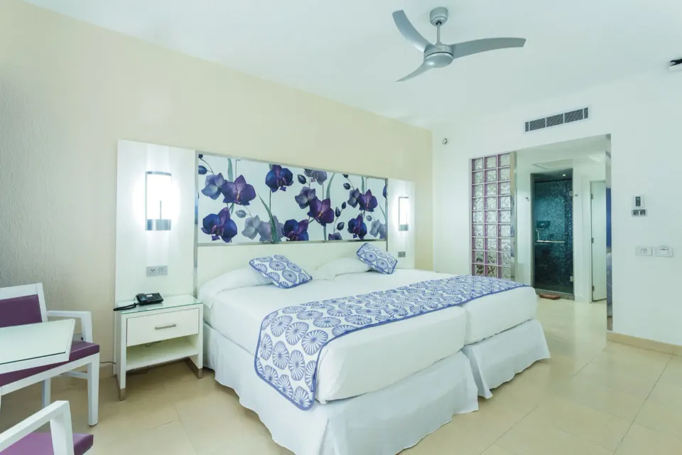 Guest room with king bed, floral headboard and en-suite bathroom at Hotel Riu Playacar.