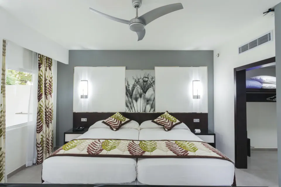 Bright guest room with two single beds pushed together and modern decor at Hotel Riu Playacar.
