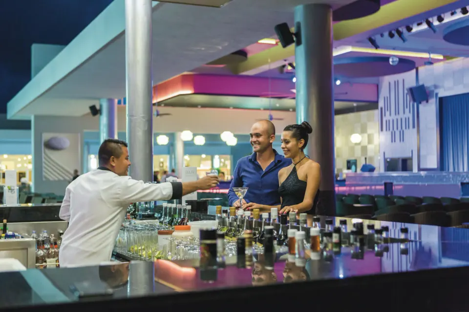 Bartender handing a drink to a couple at the bar at Hotel Riu Playacar