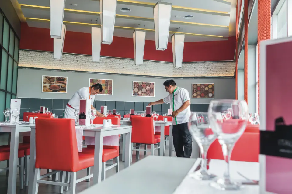 Staff setting tables in a bright red-and-white dining room at Hotel Riu Playacar