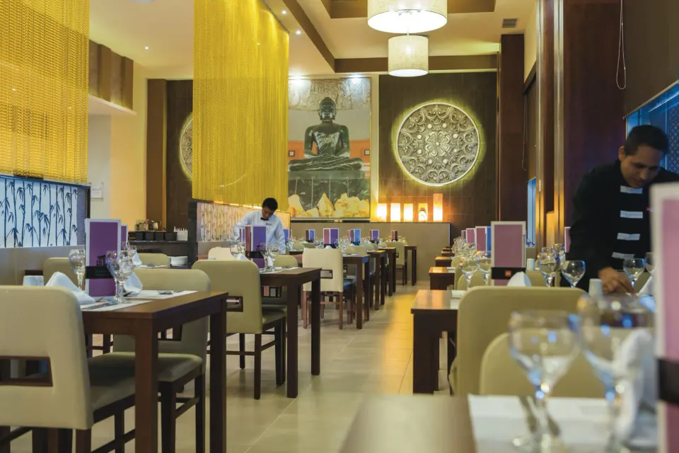 Rows of tables and place settings beneath chandeliers in the Asian restaurant at Hotel Riu Playacar.
