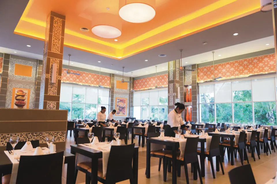 Bright dining room with white place settings and staff at Hotel Riu Playacar.