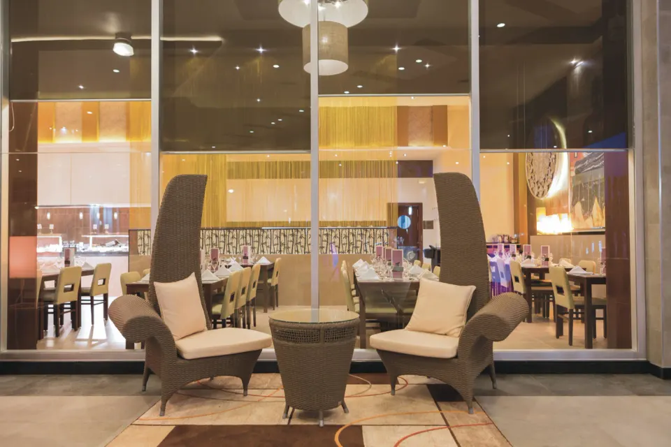 Outdoor lounge seating in front of a large window looking into a dining room at Hotel Riu Playacar