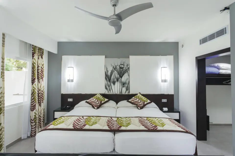 Front-on view of twin beds and headboard artwork in a Junior Suite at Hotel Riu Playacar