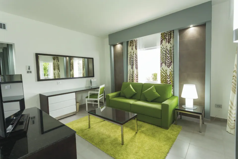 Junior Suite lounge area with green sofa, desk and TV at Hotel Riu Playacar