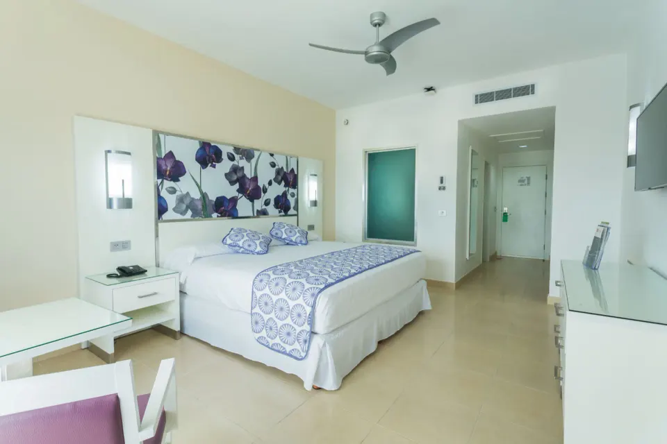 Bright guest room with a king bed and floral headboard at Hotel Riu Playacar