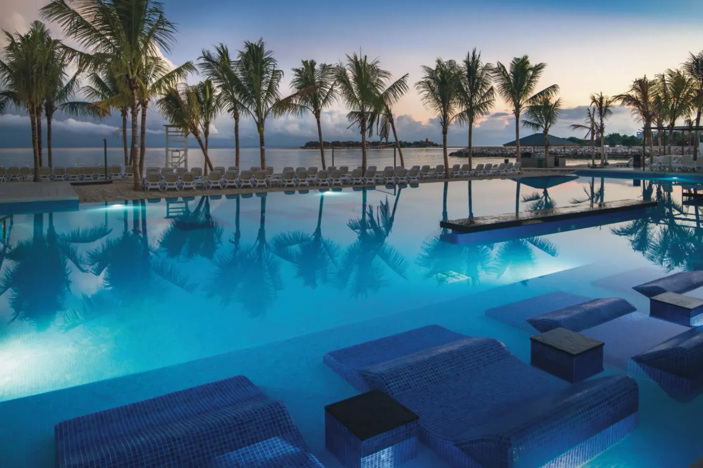 Illuminated pool with palm reflections beside the beach at Hotel Riu Reggae.
