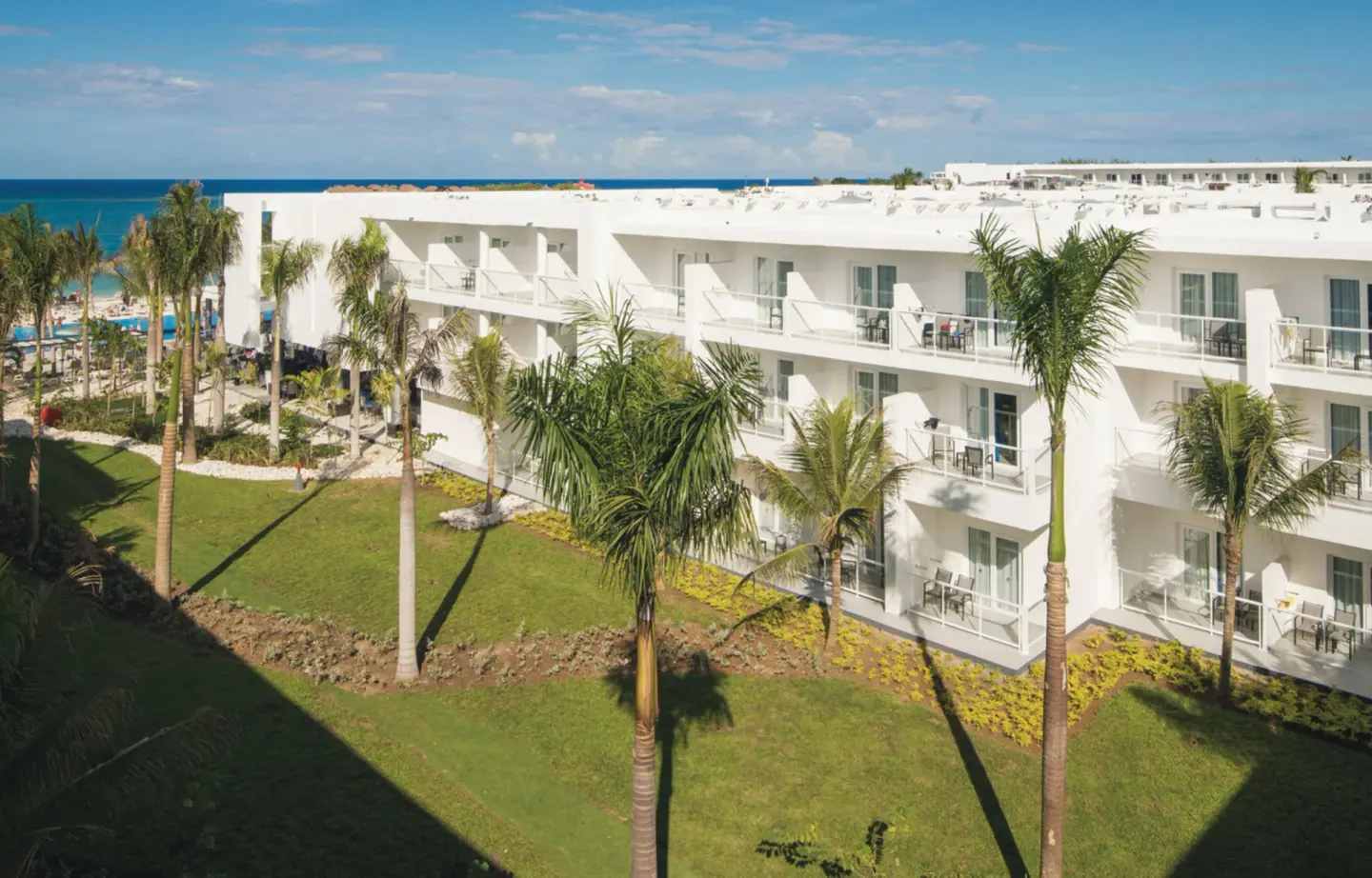 White guest room building with balconies and palms at Hotel Riu Reggae.