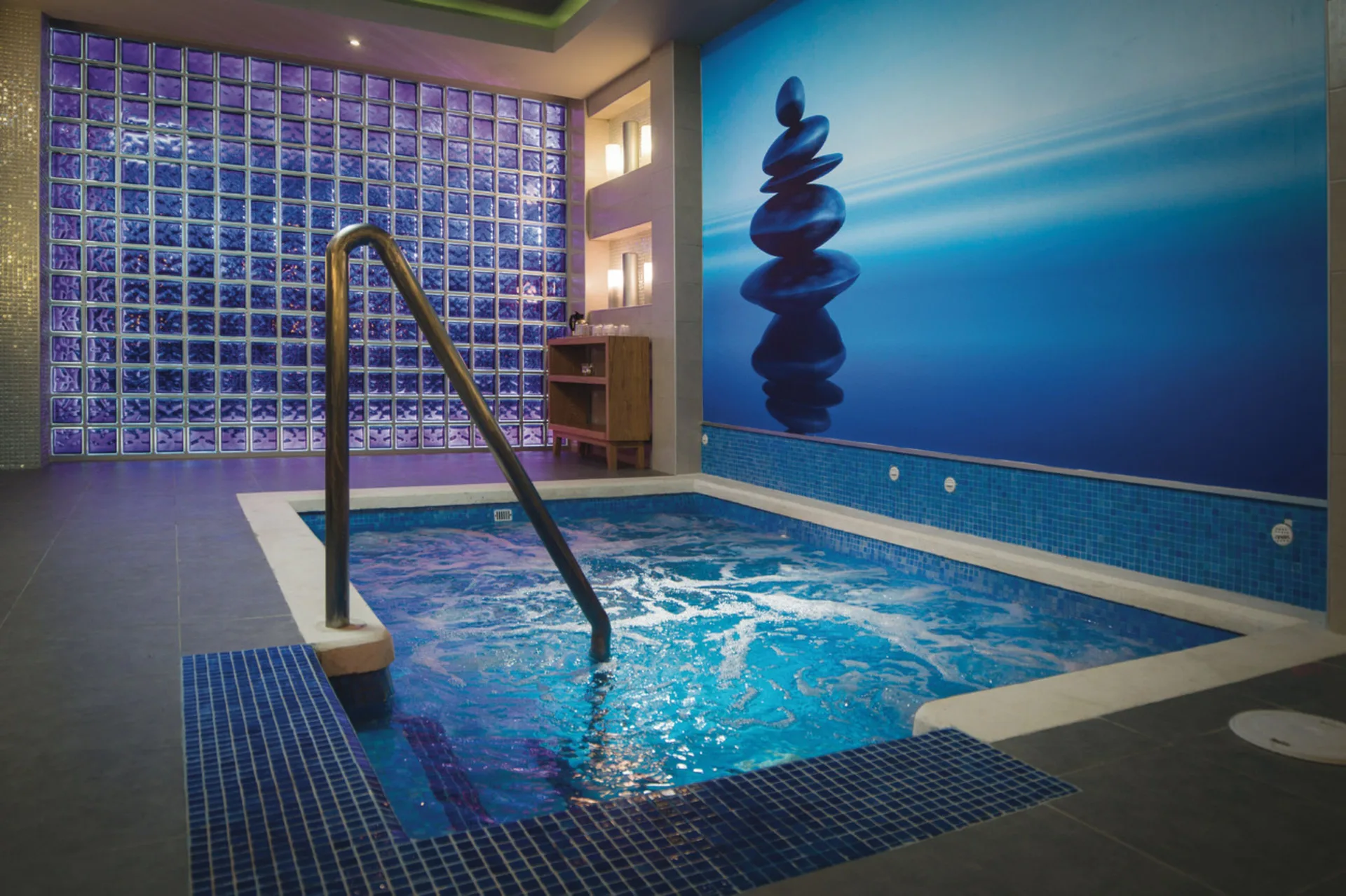 An indoor whirlpool with blue tile, glass block walls, and a metal handrail at Hotel Riu Reggae.