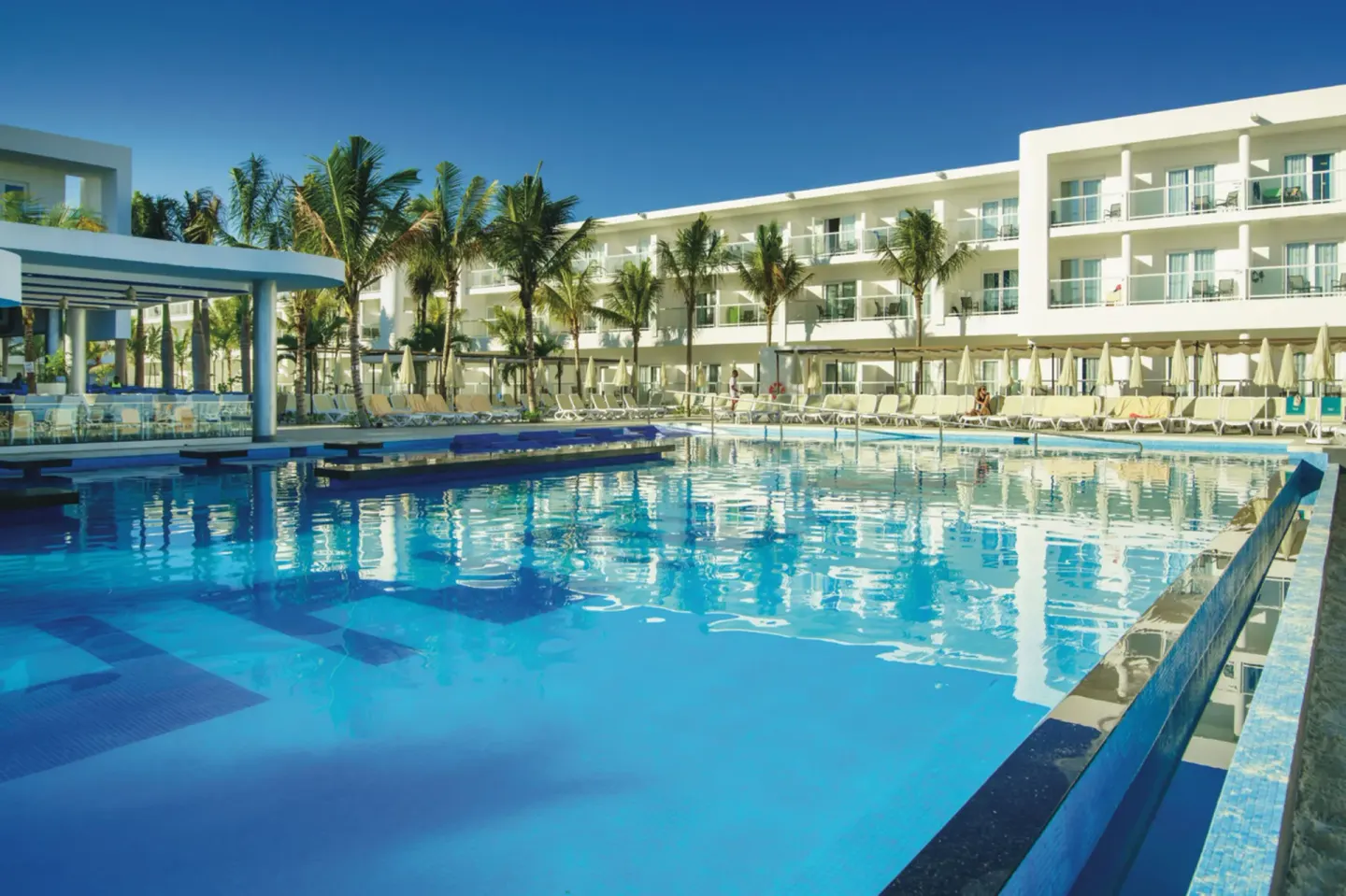 Main pool with loungers and white guest-room buildings at Hotel Riu Reggae.