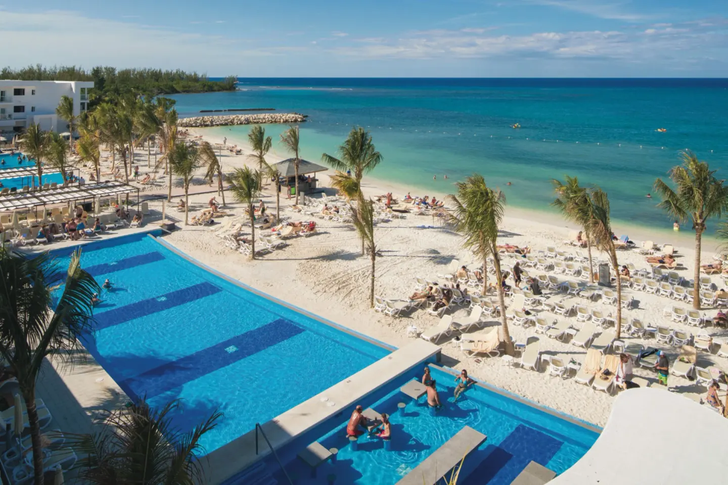 Aerial view of the pool, beach, and turquoise sea at Hotel Riu Reggae.