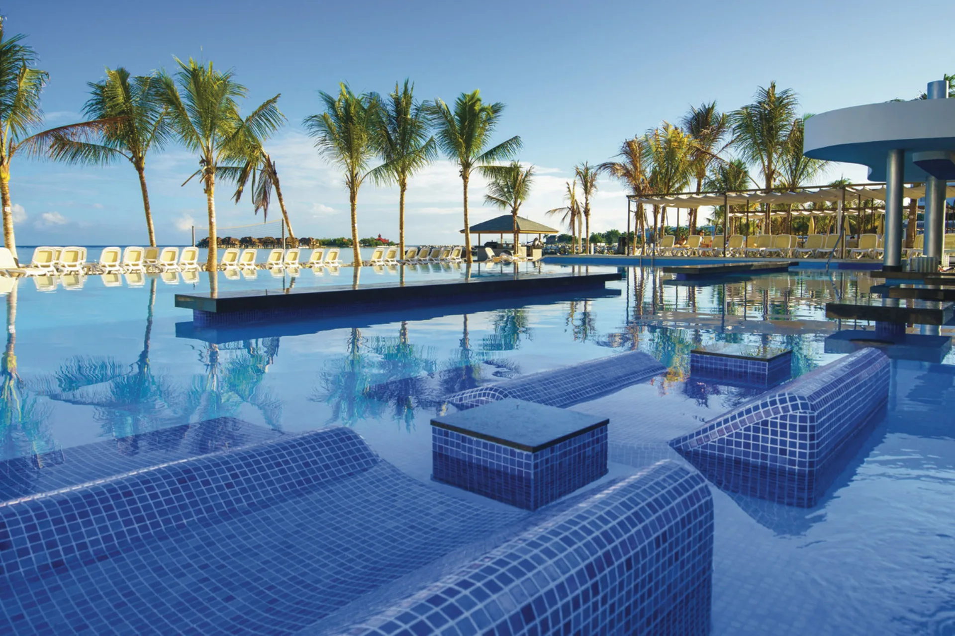 Reflective pool at Hotel Riu Reggae with in-water loungers, palms, and ocean views.