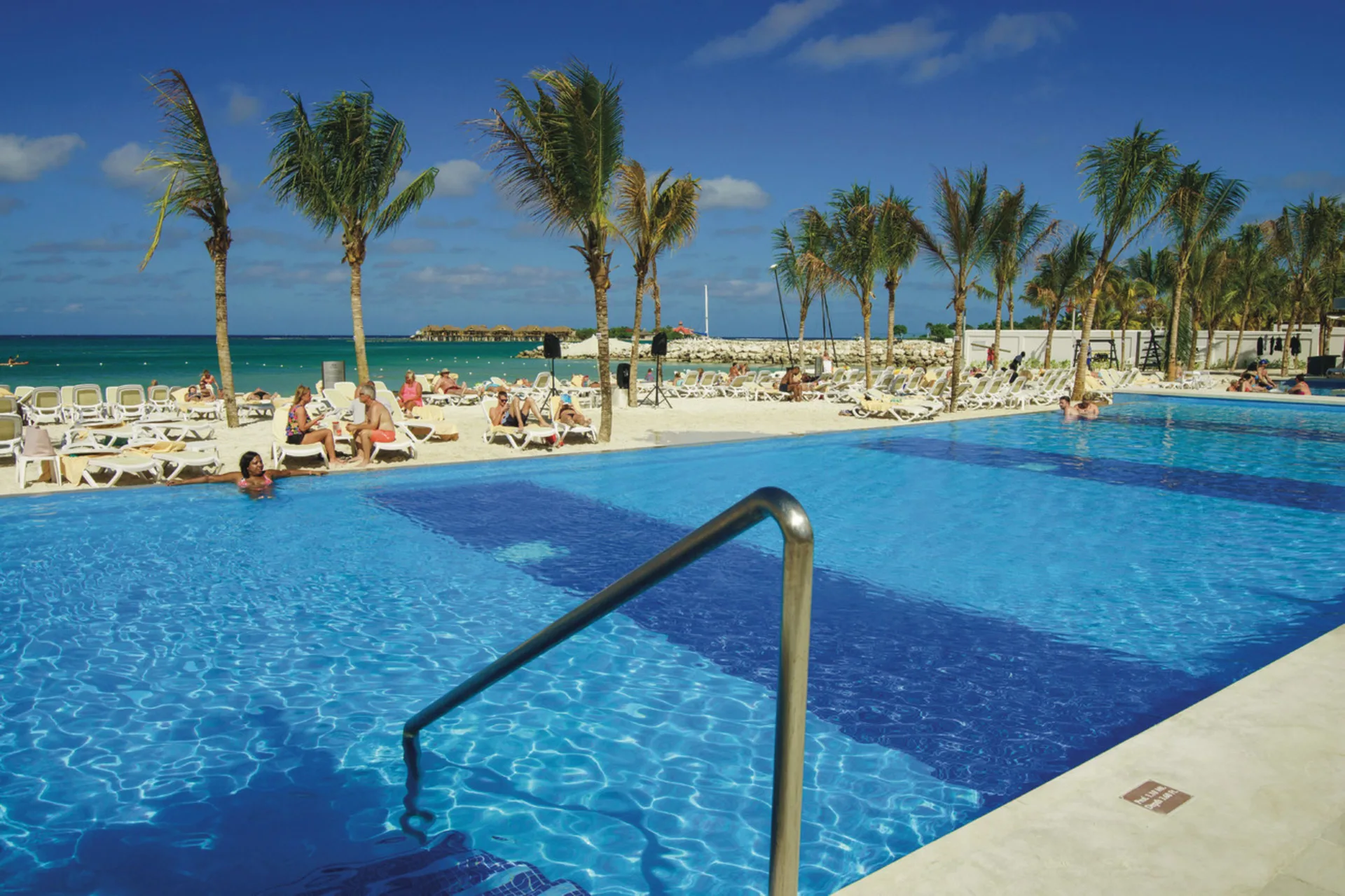Pool steps at Hotel Riu Reggae facing a palm-lined beach and blue ocean.
