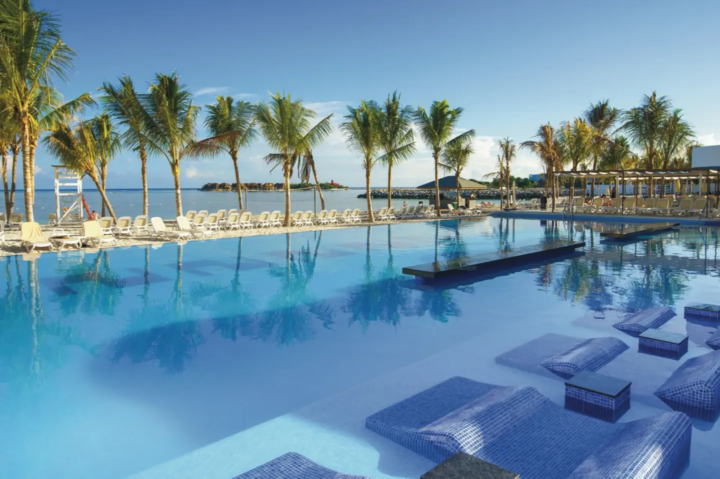 Pool with in-water loungers, palms, and beach chairs at Hotel Riu Reggae.